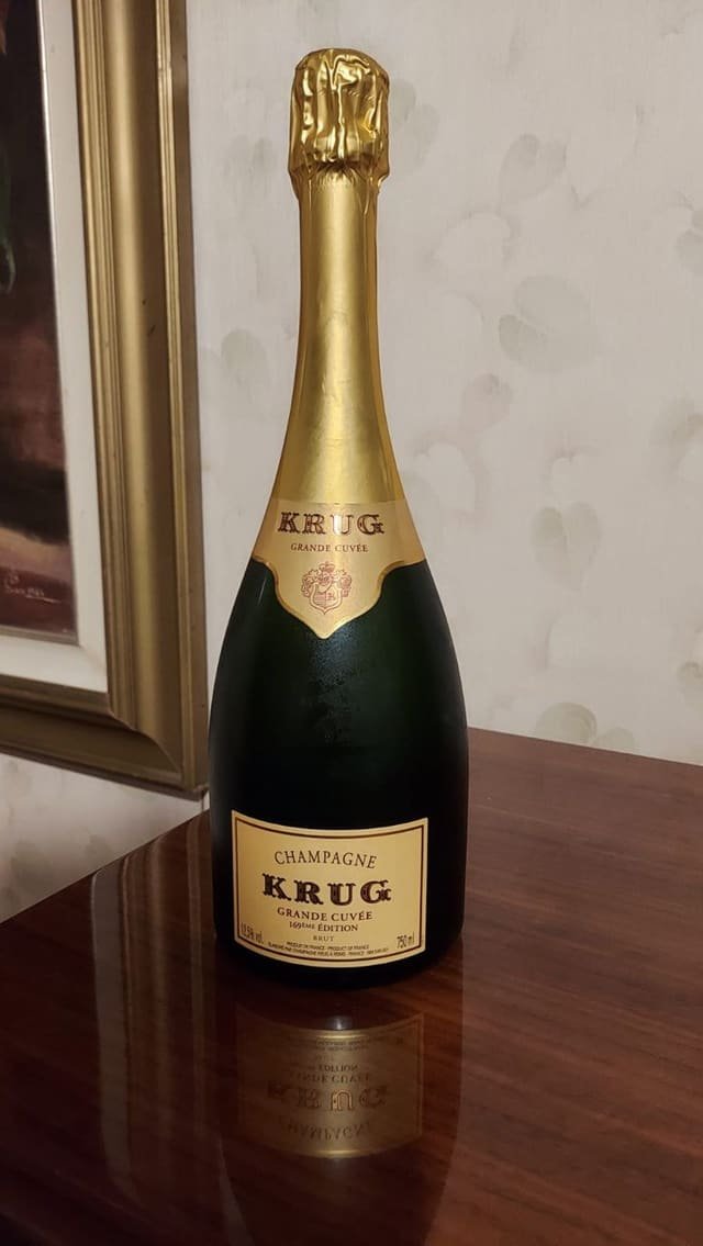 Bottiglia di Champagne Krug Grande Cuvée con la capsula dorata, su un tavolo di legno lucido