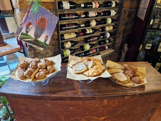 Tre alzate di vetro con polpette e fritti sulla credenza di legno, rastrelliera dei vini sullo sfondo