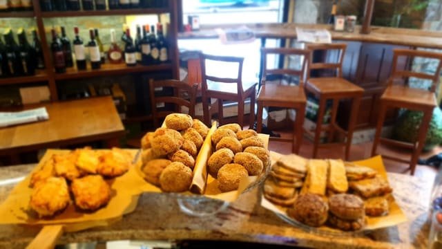 Fritti e polpette appena messi sul bancone di marmo; sullo sfondo la sala con i tavoli di legno, gli sgabelli alti e la luce che entra dalla porta