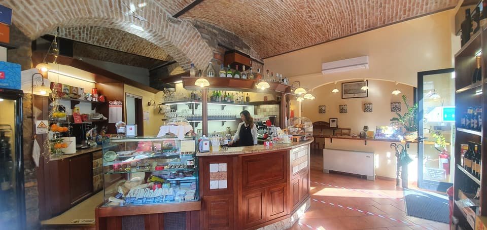Il bancone in legno della Caffetteria Villa Bousquet sotto la volta in mattoni a vista, con la vetrina dei panini e le bottiglie sulla mensola