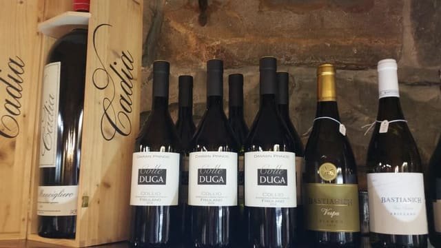 Bottiglie in piedi contro il muro di pietra: tre Colle Duga Collio Friulano, un Bastianich Vespa Bianco e un Bastianich Friulano
